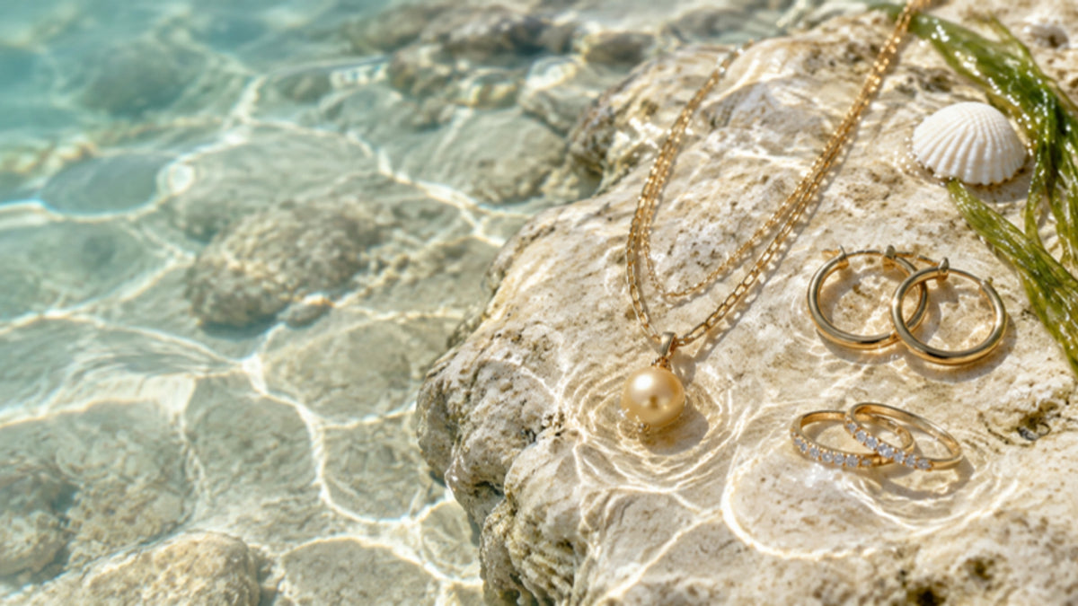 Gold layered necklace with pearl pendant, hoop earrings and stacking rings resting in a sunlit tide pool