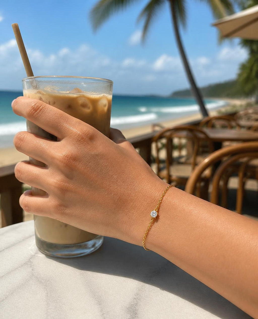 Solitaire Chain Bracelet on a wrist holding iced coffee at a beach café