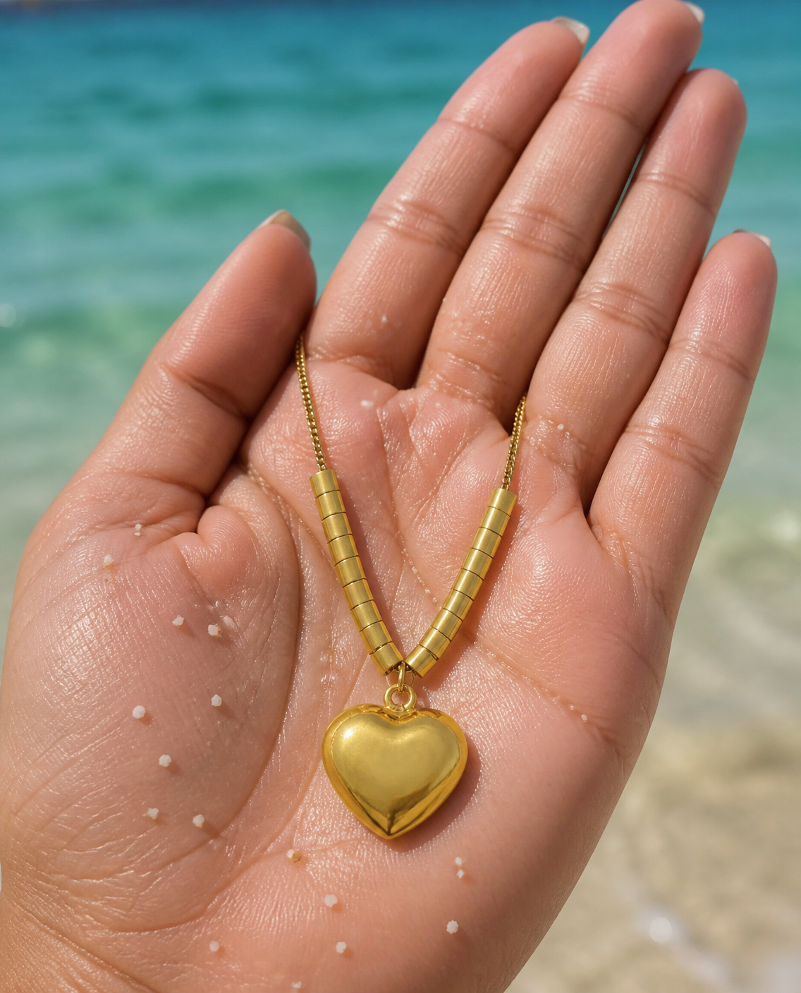 Golden Heart Pendant Necklace held in an open palm by the sea