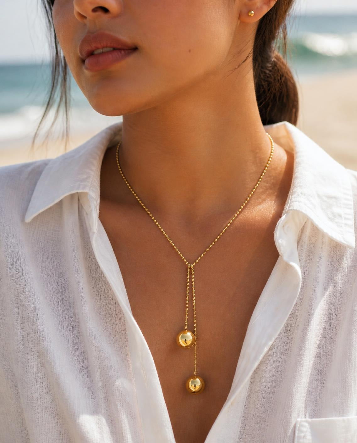 Model wearing the Gold Ball Lariat Necklace with an open linen shirt