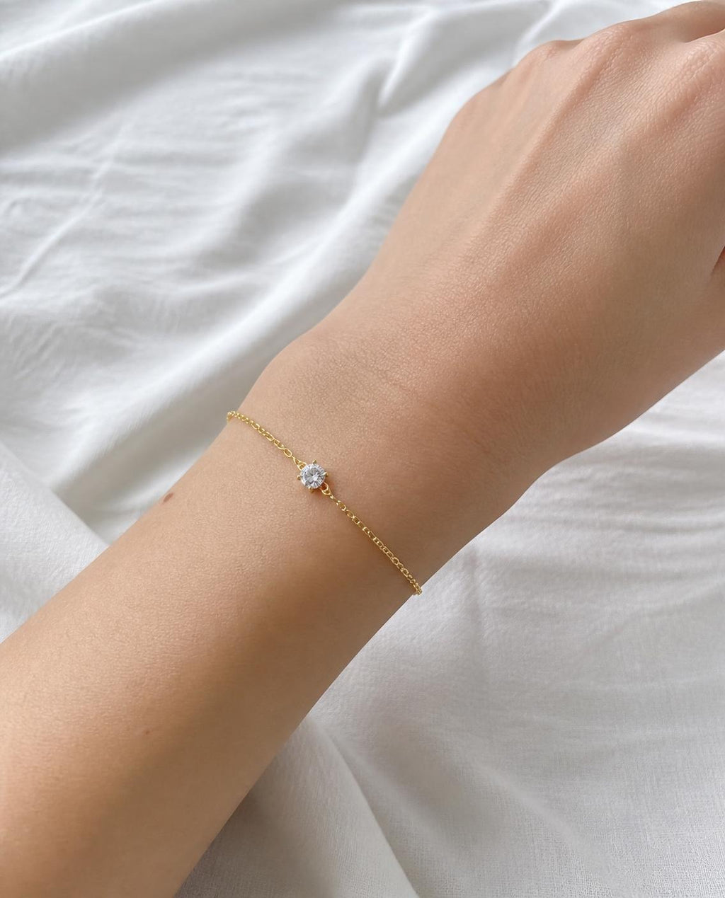 Solitaire Chain Bracelet worn on the wrist over white linen